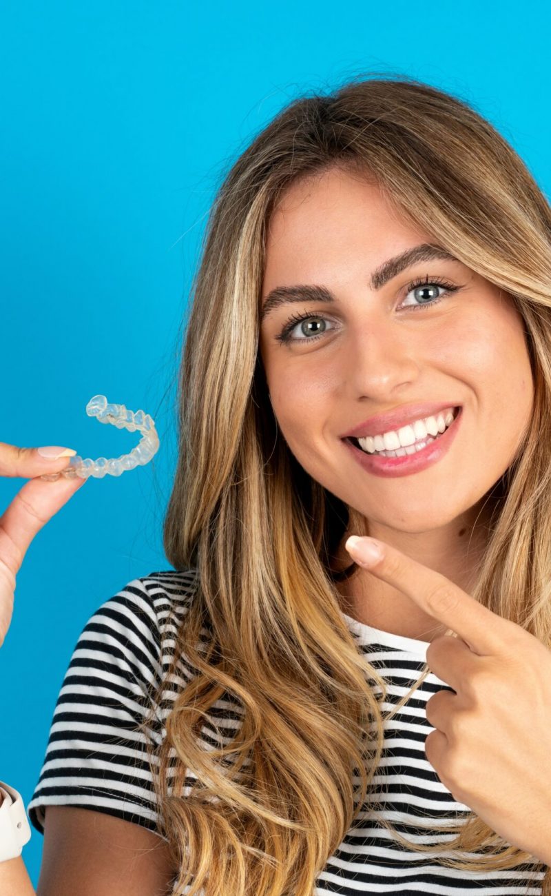 MODEL holding an invisible aligner and pointing at it. Dental healthcare and confidence concept.